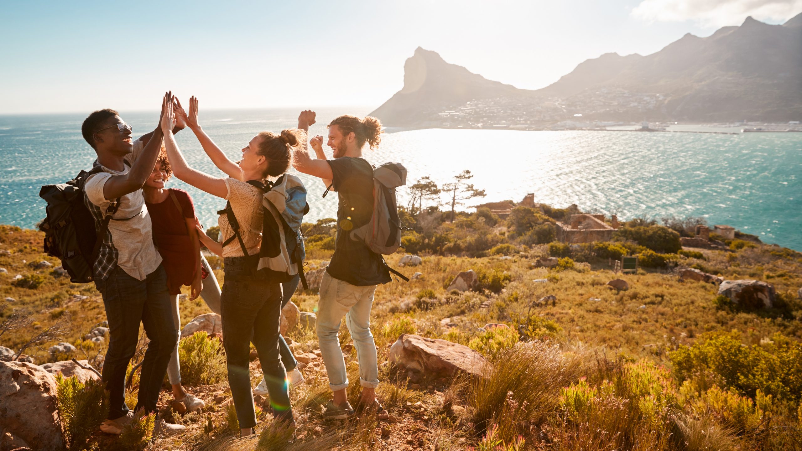 Young adult friends on a hike celebrate reaching a summit near the coast, full length, side view